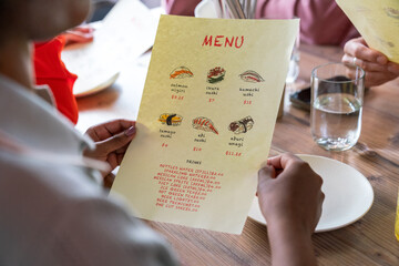 Hands Holding Sushi Menu at Cafe Table