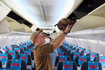 Passenger storing bag in overhead compartment on airplane