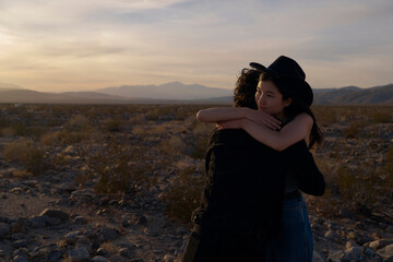 Couple Embraces in a Desert at Sunset With Mountains in the Background