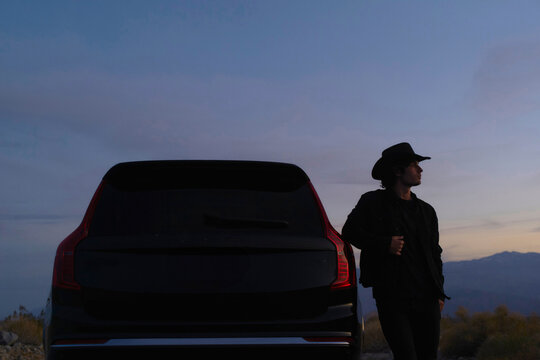 Person in Cowboy Hat Standing by Vehicle at Dusk in the Desert