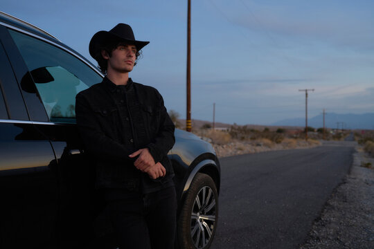 Cowboy Standing Beside Black SUV on a Quiet Rural Road at Dusk