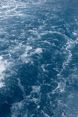 Waves ripple across a vibrant blue ocean during a clear day near a tropical shoreline