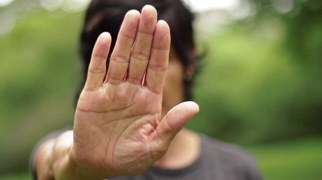 An Isolated Human Hand in a Stop Gesture on an Outdoor Background with Blurred Greenery