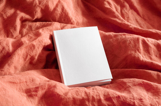 Empty white book cover mockup on red bedding 