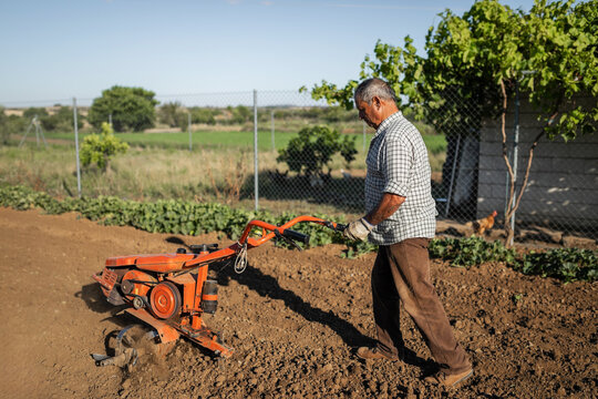 senior man tilling soil with electric cultivator