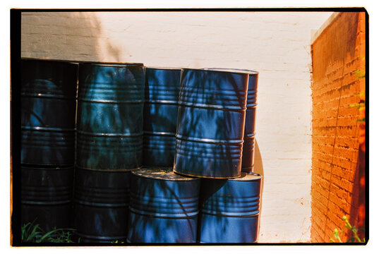 Stacked blue barrels against a textured white wall in sunlight