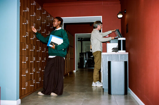 Woman using locker while man operating printer in office hallway