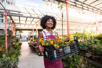 Woman Working in Garden Center Holding Crate of Flowers