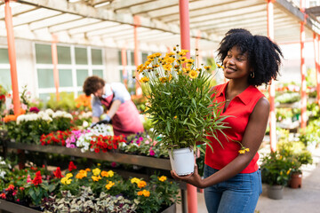 Woman holding yellow flowers in pot at garden center