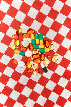 Various Pills Scattered on red and white checkered Fabric. 
