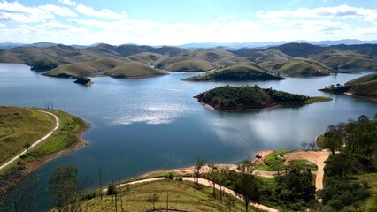 Obraz premium Impressionante paisagem aérea de barragem rodeada por colinas verdes e céu azul, perfeita para projetos turísticos e naturais.
