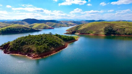 Fototapeta premium Impressionante paisagem aérea de barragem rodeada por colinas verdes e céu azul, perfeita para projetos turísticos e naturais.