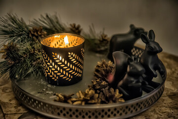 A cozy winter composition on a tray: a burning candle in a carved metal candlestick with a pattern 