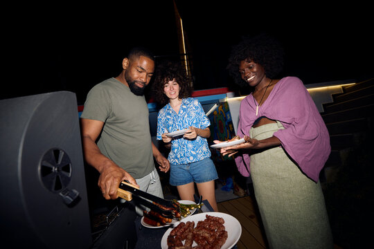 Man serves food from the grill to his friends