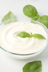 Tasty yoghurt with basil in bowl on white table, closeup