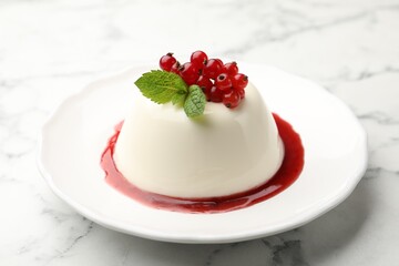 Delicious panna cotta with red currants, sauce and mint on white marble table, closeup