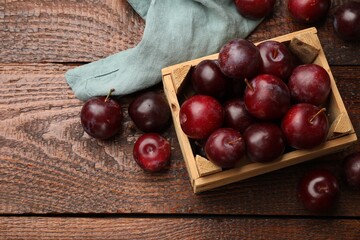Ripe cherry plums and crate on wooden table, flat lay