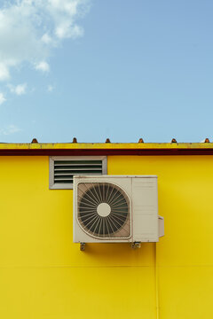 Outdoor air conditioner and vent on yellow wall under clear sky