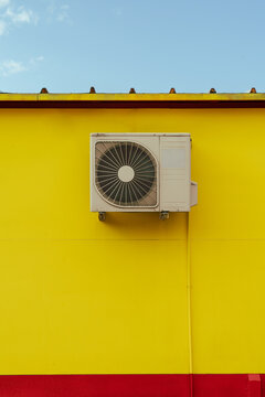 Bright yellow building exterior with roof and air conditioner