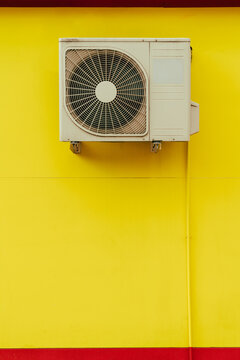 White air conditioning outdoor unit on yellow wall with cable