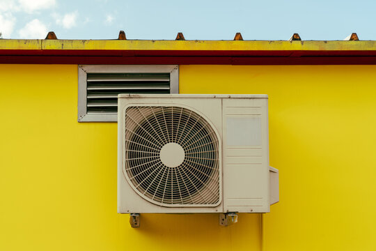 Outdoor air conditioner and vent on yellow wall under metal roof
