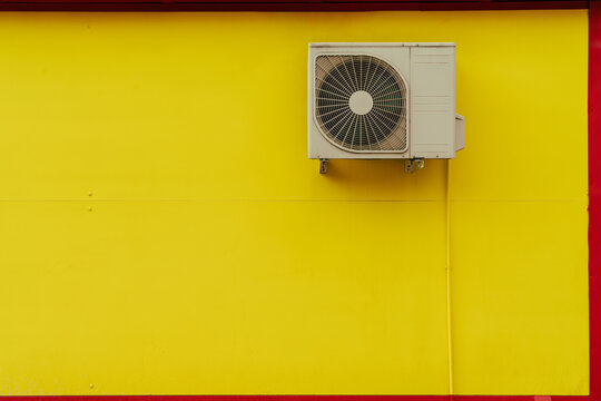 HVAC outdoor unit on vibrant yellow wall with red accent