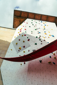 Tall outdoor climbing wall with colorful holds under cloudy sky