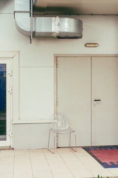 Transparent chair near industrial ventilation duct and white door