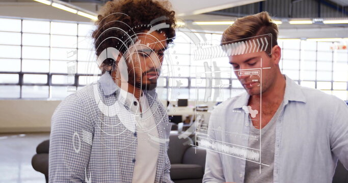 Reviewing metrics two colleagues wearing shirts using digital interface in office, with charts