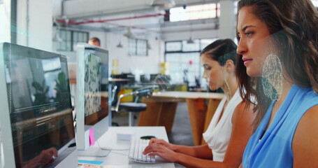Obraz premium Working two women in sleeveless tops typing on monitors at desk in open-plan office, copy space
