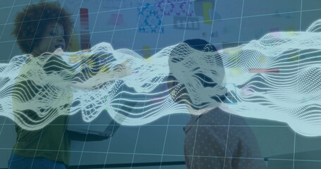 Collaborating women wearing casual tops holding laptop pointing at whiteboard in office, with wave