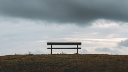 Empty park bench on a grassy hilltop under a cloudy sky.