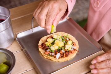Detail of the hands of an unrecognizable elderly woman eating tacos al pastor