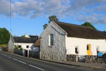 Fototapeta premium Stone cottages painted white, included one with a thatched roof, close to a road in Kinvara, County Galway, Ireland