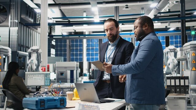 Diverse team of engineers and specialists collaborate in a solar panel factory, review blueprints and share ideas to enhance renewable energy production and sustainable innovation. Camera A.