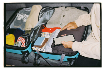 A man packs his suitcase by checking a list on his phone.
