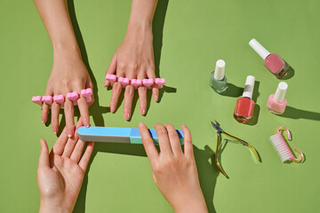 Manicure in progress with hands, tools, and nail polish on green