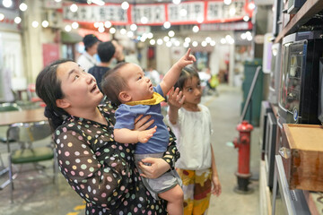 Fototapeta premium In an old-town-style mall, a Chinese family enjoys the day; a one-year-old in a stroller and kids under ten chat as adults in their thirties gather to watch old televisions. Shanghai, China. Spring.