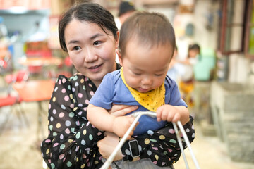 Inside an old town style mall, a Chinese family gathers at a kitchen set; a one year old in a...