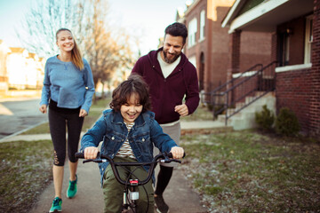 Parents teaching young son how to ride a bike outside
