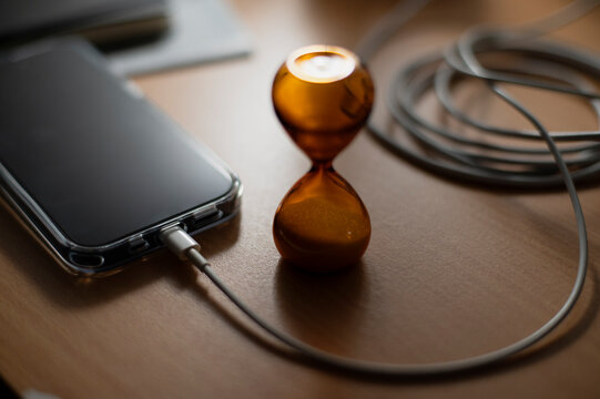 Smartphone charging beside small amber hourglass