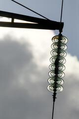Obraz premium This striking image captures a close-up of glass insulators on a high-voltage power line against a cloudy sky, with sunlight creating a dramatic effect.