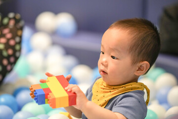 A 1 year old Chinese baby plays with colorful blocks in a pool of plastic balls at an indoor play area. Hongkou District, Shanghai, China. Spring.