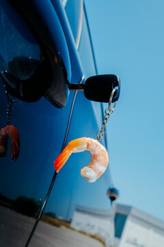 car key with a peeled shrimp keychain hanging from it, on a parked car