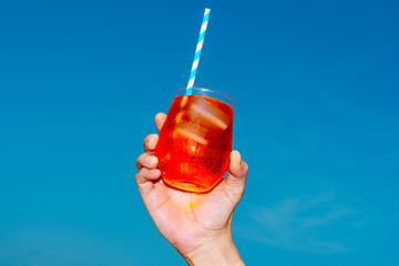 man holds a glass of spritz under a clear blue sky