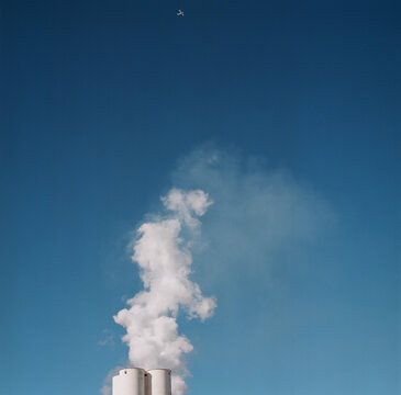 Steam Rising from Silos Under Passing Plane
