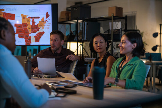 Business team meeting late night at office, reviewing data on a screen