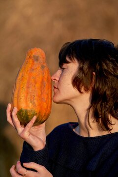 Person smells orange pumpkin close to face during golden hour