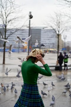 Woman in green top and plaid skirt interacts with pigeons city