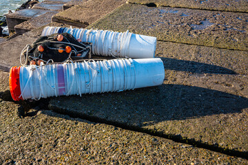 Two groups of empty paint buckets used to carry the fish caught with the net placed between them. The scene, captured on a concrete pier, highlights artisanal fishing practices and the practical reuse